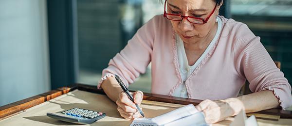 Woman at a desk, with calculator, looking at spreadsheets
